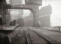 687_B_327 Hafenarbeiter transportieren abgeladene Wollballen von der Rampe in den Kaischuppen zur Lagerung. Unter den Portalkrnen steht ein Gterzug an der Laderampe - der hohe Bug eines Frachters ist im Nebel des Hamburger Hafens am Kai zu erkennen.