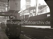 689_B_327a ber einen Kesselwagen der Hamburger Hafenbahn werden mit einem dicken Schlauch die Tanks des Frachtschiffs befllt. ber den Kran wird der Schlauch in seiner Position gehalten, ein Arbeiter kontrolliert den Vorgang.