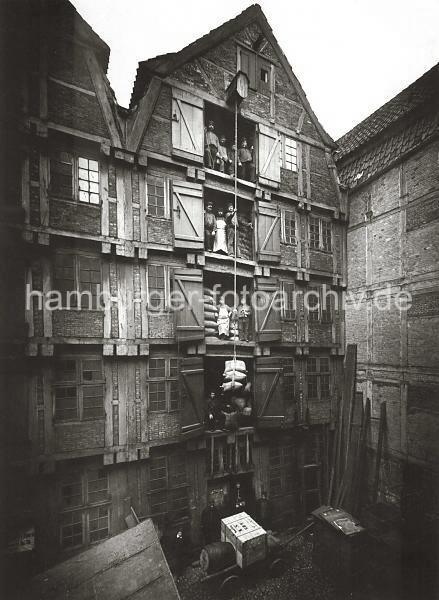 0112_3501_47 Historisches Speichergebude am ALTEN WANDRAHM im Gebiet der zuknftigen Speicherstadt - Lagerarbeiter stehen bei geffneten Luken auf den unterschiedlichen Lagerbden; im Hintergrund sind Scke gestapelt. ber eine Winde, die unter dem Dach des Fachwerkgebudes angebracht ist, wird eine Hieve Scke transportiert. Auf dem Kopfsteinpflaster des Hofs steht eine Handkarre, die mit einer grossen Holzkiste und einem Fass beladen ist. Ab 1883 wurden die Wohnviertel auf den Elbinseln Kehrwieder und Wandrahm abgerissen, um die Speicherstadt zu errichten. Etwa 20 000 Menschen wurden zwangsumgesiedelt, ca. 1100 Huser wurden zerstrt.