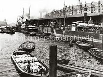 0142_233_1 Blick in den Sandtorhafen - Frachter liegen am Kai; Binnenschiffe und Schuten haben lngsseits fest gemacht. Im Vordergrund bewegen zwei Ewerfhrer ihre mit Holzkisten beladenen Schuten mit dem Peekhaken / Bootshaken durch das Hafenbecken. Links im Hintergrund ist der Kaiserspeicher zu erkennen und re. zwischen den neogotischen Giebeln der Speicherstadt am Sandtorkai die qaulmenden Schornsteine des Kesselhauses. Die Hamburger Speicherstadt wurde ab 1883 errichtet. Dabei wurden zunchst die ab dem 16. Jahrhundert auf den Elbinseln Kehrwieder und Wandrahm gewachsenen Wohnviertel abgerissen. Der Kehrwieder galt als Arbeiter- und Handwerkerviertel mit teilweise enger Gngeviertelbebauung, der Wandrahm war vor allem mit Kaufmanns- und Brgerhusern aus dem 17. und 18. Jahrhundert bebaut und insbesondere von hollndischen Einwanderern geprgt. Die Realisierung und Verwaltung der Speicherstadt wurde im Jahr 1885 durch die Hamburger Freihafen-Lagerhaus-Gesellschaft (HFLG) bernommen. Bis 1889 entstanden zwischen Kehrwiederspitze und Kannengieerort etwa 60 Prozent der Lagerflchen (Blcke A bis O). Im zweiten Bauabschnitt von 1891 bis 1897 wurden die Speicherblcke P, Q und R am St. Annenufer und Neuer Wandrahm errichtet. Im dritten Bauabschnitt von 1899 bis 1927, unterbrochen durch den Ersten Weltkrieg und die Inflationsjahre, wurde das Gebiet stlich der Strae Bei St. Annen fertig gestellt (Blcke S bis X). Das "Rathaus" der Speicherstadt, das Verwaltungsgebude der HHLA, wurde 1903 eingeweiht. Insgesamt entstanden 24 Speicherblcke mit rund 300.000 Quadratmeter Lagerflche.