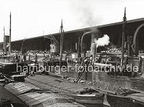 0143_230_2 Blick in den Grasbrookhafen - abgedeckte Binnenschiffe mit eigenem Steuerruder liegen im Hafenbecken des Grasbrookhafens. ber eine mit Kohle beladene Schute transportieren Arbeiter die Kohle in Krben ber eine Leiter an Deck eines Dampfschiffs. Im offenen Lagerraum des Kaischuppens sind gestapelte Fsser zu erkennen; davor laufen Dampfkrane und Rollkrane auf Schienen. 1868 wurde als erstes knstliches Hafenbecken der Sandtorhafen ausgehoben. Die neugeschaffenen Kaianlagen des nrdlichen Sandtorkais bestanden aus hlzernen Bollwerken, spter beim 1872 fertiggestellten Kaiserkai aus  Klinkern, an der die Seeschiffe direkt anlegen konnten. Sie verfgten meistens ber parallel zur Kaikante auf Schienen bewegliche Krananlagen fr den Stckgutumschlag, ber Eisenbahnanschluss sowie einfache Kaischuppen, die dem Sortieren, nicht aber dem Lagern von Waren dienten. Dies ermglichte zum ersten Mal einen direkten Warenumschlag in Bahnwaggons oder Fuhrwerke und galt seinerzeit als das modernste Umschlagsystem der Welt. Binnen weniger Jahre erfolgte der Bau weiterer Hafenbecken auf dem Groen Grasbrook, so des (1876), des Magdeburger Hafen (ab 1872) und des Brooktorhafen (um 1880) mit einem Durchlass zwischen beiden, 1881 kam der Grasbrookhafen hinzu.