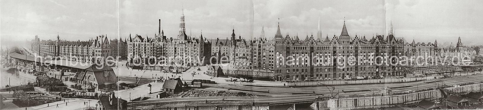 0146_17 Panorama der historischen Hamburger Speicherstadt - Blick ber den Brooktorhafen zu den Speichergebuden am Sandtor (lks.) und Brooktor (re.). Im Bildzentrum der St. Annenplatz, rechts davon das Verwaltungsgebude (Speicherstadt-Rathaus) der HFLG. Hinter den Neogotischen Giebeltrmen der Speichergebude die Trme der Hansestadt Hamburg. Die Hamburger Speicherstadt wurde ab 1883 errichtet. Dabei wurden zunchst die ab dem 16. Jahrhundert auf den Elbinseln Kehrwieder und Wandrahm gewachsenen Wohnviertel abgerissen. Der Kehrwieder galt als Arbeiter- und Handwerkerviertel mit teilweise enger Gngeviertelbebauung, der Wandrahm war vor allem mit Kaufmanns- und Brgerhusern aus dem 17. und 18. Jahrhundert bebaut und insbesondere von hollndischen Einwanderern geprgt. Die Realisierung und Verwaltung der Speicherstadt wurde im Jahr 1885 durch die Hamburger Freihafen-Lagerhaus-Gesellschaft (HFLG) bernommen. Bis 1889 entstanden zwischen Kehrwiederspitze und Kannengieerort etwa 60 Prozent der Lagerflchen (Blcke A bis O). Im zweiten Bauabschnitt von 1891 bis 1897 wurden die Speicherblcke P, Q und R am St. Annenufer und Neuer Wandrahm errichtet. Im dritten Bauabschnitt von 1899 bis 1927, unterbrochen durch den Ersten Weltkrieg und die Inflationsjahre, wurde das Gebiet stlich der Strae Bei St. Annen fertig gestellt (Blcke S bis X). Das "Rathaus" der Speicherstadt, das Verwaltungsgebude der HHLA, wurde 1903 eingeweiht. Insgesamt entstanden 24 Speicherblcke mit rund 300.000 Quadratmeter Lagerflche.