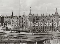 0146_17 Panorama der historischen Hamburger Speicherstadt - Blick ber den Brooktorhafen zu den Speichergebuden am Sandtor (lks.) und Brooktor (re.). Im Bildzentrum der St. Annenplatz, rechts davon das Verwaltungsgebude (Speicherstadt-Rathaus) der HFLG. Hinter den Neogotischen Giebeltrmen der Speichergebude die Trme der Hansestadt Hamburg. Die Hamburger Speicherstadt wurde ab 1883 errichtet. Dabei wurden zunchst die ab dem 16. Jahrhundert auf den Elbinseln Kehrwieder und Wandrahm gewachsenen Wohnviertel abgerissen. Der Kehrwieder galt als Arbeiter- und Handwerkerviertel mit teilweise enger Gngeviertelbebauung, der Wandrahm war vor allem mit Kaufmanns- und Brgerhusern aus dem 17. und 18. Jahrhundert bebaut und insbesondere von hollndischen Einwanderern geprgt. Die Realisierung und Verwaltung der Speicherstadt wurde im Jahr 1885 durch die Hamburger Freihafen-Lagerhaus-Gesellschaft (HFLG) bernommen. Bis 1889 entstanden zwischen Kehrwiederspitze und Kannengieerort etwa 60 Prozent der Lagerflchen (Blcke A bis O). Im zweiten Bauabschnitt von 1891 bis 1897 wurden die Speicherblcke P, Q und R am St. Annenufer und Neuer Wandrahm errichtet. Im dritten Bauabschnitt von 1899 bis 1927, unterbrochen durch den Ersten Weltkrieg und die Inflationsjahre, wurde das Gebiet stlich der Strae Bei St. Annen fertig gestellt (Blcke S bis X). Das "Rathaus" der Speicherstadt, das Verwaltungsgebude der HHLA, wurde 1903 eingeweiht. Insgesamt entstanden 24 Speicherblcke mit rund 300.000 Quadratmeter Lagerflche.