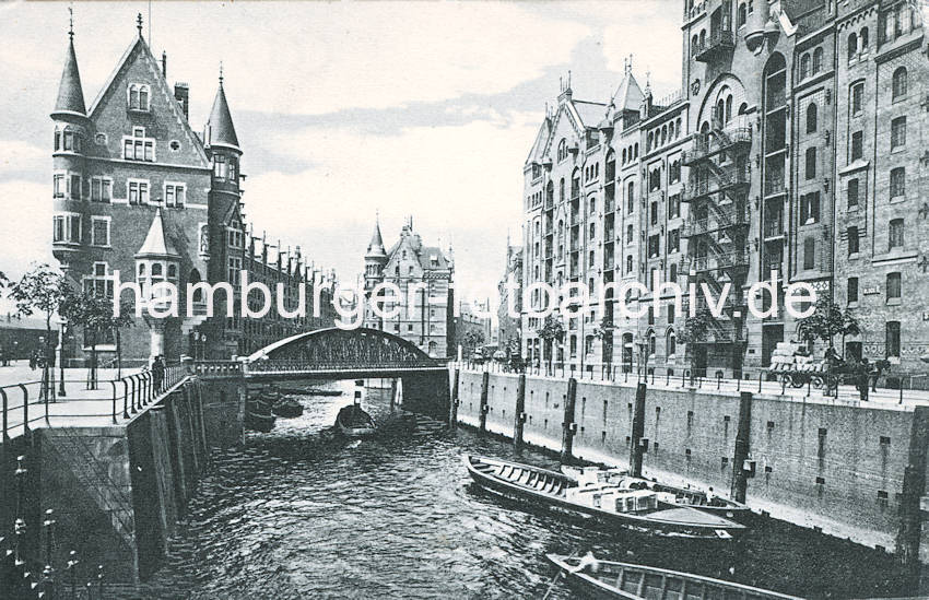 0150_18_1139  Blick ber das St Annenfleet zur Neuerwegsbrcke und das dahinterliegende Brooksfleet. Beladene Schuten liegen am Kai des St. Annenufer; ein Ewerfhrer stakt mit seinem Bootshaken seinen Kahn ber den Kanal - ein Schlepper unterquert die Brcke und fhrt in das Brooksfleet ein. Ein Pferdefuhrwerk transportiert Scke auf der Strasse St. Annenufer vor dem Speicher von Hanssen & Stude. Lks. das ursprngliche Direktionsgebude der Speicherstadtverwaltung / Hamburger Freihafen-Lagerhaus-Gesellschaft (HFLG) - in der Bildmitte hinter dem Brckenbogen das Speichergebude G. 