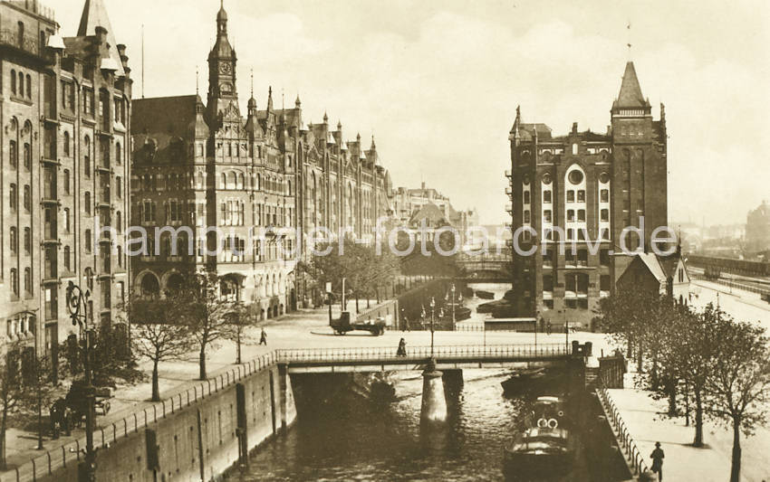 0150_17_1_30  Im Vordergrund die St. Annenbrcke ber das St. Annenfleet / Hollndischbrookfleet - Gaslaternen mit drei schmiedeeiserne Lampen steht in der Mitte der Brcke. Am St. Annen / Hollndischer Brook liegt das grosse Verwaltungsgebude der Hamburger Freihafen-Lagerhaus-Gesellschaft HFLG, das mit seinen vielen neogotischen Giebeltrmen auch das Speicherstadtrathaus genannt wird. Dahinter schliesst der Speicherblock U an, der mit seiner Wasserseite am Wandrahmsfleet liegt. Rechts der Speicherblocks V, davor ein Gebude der Speicherstadt-Feuerwache. Am rechten Bildrand Gleise der Hafenbahn sowie ein Gterwaggon. 