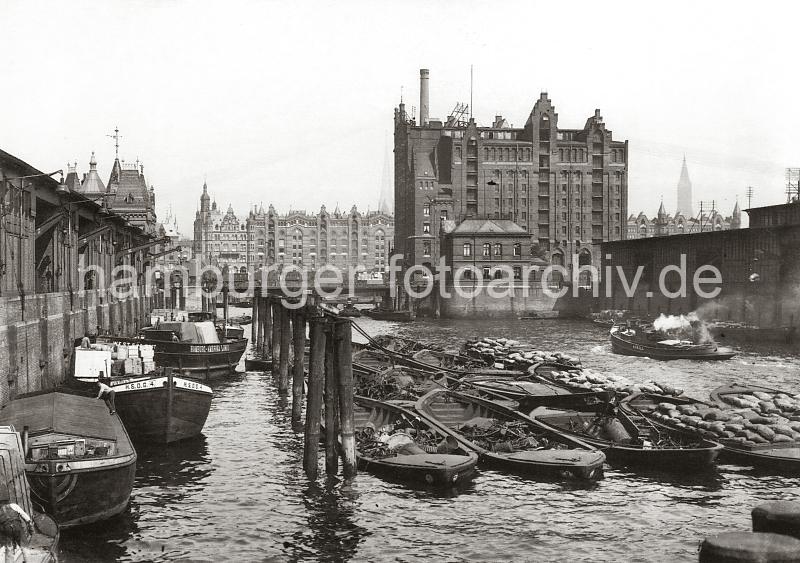 0155_228_2 Blick von der Baakenbrcke auf den Magdeburger Hafen - Schuten und Binnenschiffe liegen am Kai unter den Winden der Fruchtschuppen. Am Bug eines der Lastkhne ist das Logo der Hamburg - Sdamerikanische Dampfschifffahrts-Gesellschaft H.S.D.G. angebracht und an der Bordwand eines anderen Schiffs ist der Schriftzug "Hamburg Amerika Linie" zu erkennen. An den Dalben des Hafenbeckens wird Schrott in Schuten gelagert, ein Arbeitsschiff fhrt unter Dampf Richtung Magdeburger Brcke; rechts der Kaispeicher B, davor das Brckenwrterhaus - im Hintergrund die Speicherblcke am Brooktorkai. 1868 wurde als erstes knstliches Hafenbecken der Sandtorhafen ausgehoben. Die neugeschaffenen Kaianlagen des nrdlichen Sandtorkais bestanden aus hlzernen Bollwerken, spter beim 1872 fertiggestellten Kaiserkai aus  Klinkern, an der die Seeschiffe direkt anlegen konnten. Sie verfgten meistens ber parallel zur Kaikante auf Schienen bewegliche Krananlagen fr den Stckgutumschlag, ber Eisenbahnanschluss sowie einfache Kaischuppen, die dem Sortieren, nicht aber dem Lagern von Waren dienten. Dies ermglichte zum ersten Mal einen direkten Warenumschlag in Bahnwaggons oder Fuhrwerke und galt seinerzeit als das modernste Umschlagsystem der Welt. Binnen weniger Jahre erfolgte der Bau weiterer Hafenbecken auf dem Groen Grasbrook, so des (1876), des Magdeburger Hafen (ab 1872) und des Brooktorhafen (um 1880) mit einem Durchlass zwischen beiden, 1881 kam der Grasbrookhafen hinzu.