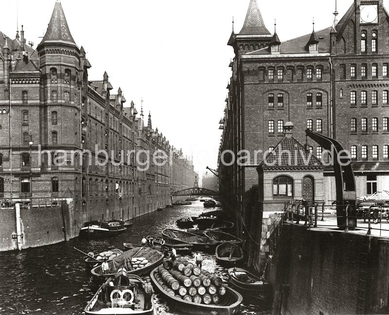 0163_3505_73 Schuten und Binnenschiffe im Kehrwiederfleet; im Hintergrund die Kehrwiederbrcke - rechts der Speicherblock J und links der Speicher A. Hinter dem Kran sind leere Handkarren geparkt. Die Schiffe haben Holzfsser und Scke geladen; einer der Ewerfhrer legt seinen Kahn mit Hilfe seines Peekhakens an die Seite einer Schute. Im Vordergrund ein Schleppschiff, der Schornstein ist herunter geklappt, damit das Arbeitsschiff unter der Wilhelminenbrcke hindurch fahren kann. An der steinernen Treppe am Kai hat ein Tuckerboot festgemacht. Die Hamburger Speicherstadt wurde ab 1883 errichtet.  Die Realisierung und Verwaltung der Speicherstadt wurde im Jahr 1885 durch die Hamburger Freihafen-Lagerhaus-Gesellschaft (HFLG) bernommen. Bis 1889 entstanden zwischen Kehrwiederspitze und Kannengieerort etwa 60 Prozent der Lagerflchen (Blcke A bis O). Im zweiten Bauabschnitt von 1891 bis 1897 wurden die Speicherblcke P, Q und R am St. Annenufer und Neuer Wandrahm errichtet. Im dritten Bauabschnitt von 1899 bis 1927, unterbrochen durch den Ersten Weltkrieg und die Inflationsjahre, wurde das Gebiet stlich der Strae Bei St. Annen fertig gestellt (Blcke S bis X). Das "Rathaus" der Speicherstadt, das Verwaltungsgebude der HHLA, wurde 1903 eingeweiht. Insgesamt entstanden 24 Speicherblcke mit rund 300.000 Quadratmeter Lagerflche.