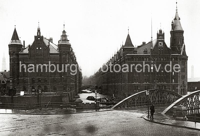 0164_090_1 Blick von der Kehrwiederspitze auf die Wilhelminenbrcke und das Kehrwiederfleet - Lastkhne liegen unter den Winden der Lagerbden. Links der Speicherblock A und rechts der Block J; eine weit sichtbare Uhr ist im Giebel des Lagergebudes angebracht. Die Hamburger Speicherstadt wurde ab 1883 errichtet.  Die Realisierung und Verwaltung der Speicherstadt wurde im Jahr 1885 durch die Hamburger Freihafen-Lagerhaus-Gesellschaft (HFLG) bernommen. Bis 1889 entstanden zwischen Kehrwiederspitze und Kannengieerort etwa 60 Prozent der Lagerflchen (Blcke A bis O). Im zweiten Bauabschnitt von 1891 bis 1897 wurden die Speicherblcke P, Q und R am St. Annenufer und Neuer Wandrahm errichtet. Im dritten Bauabschnitt von 1899 bis 1927, unterbrochen durch den Ersten Weltkrieg und die Inflationsjahre, wurde das Gebiet stlich der Strae Bei St. Annen fertig gestellt (Blcke S bis X). Das "Rathaus" der Speicherstadt, das Verwaltungsgebude der HHLA, wurde 1903 eingeweiht. Insgesamt entstanden 24 Speicherblcke mit rund 300.000 Quadratmeter Lagerflche.