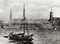 0172_236_2a Ein Fischkutter fhrt auf im Hamburger Hafen - der Steuermann des Schiffs steht im Heck; im Schlepp hat der Kutter ein Ruderboot,  Netze hngen ber die Bordwand des Holzschiffs. Auf der Norderelbe fahren Barkassen und ein Schlepper; schwarzer Qualm kommt aus dem Schornstein des Arbeitsschiffs. Im Hintergrund Kirchtrme der Hansestadt, sowie Rathausturm und die Neogotischen Giebeltrme der Speicherstadt - rechts der Uhrenturm des Kaiserspeichers - in seinem inneren befindet sich eine feuersichere Treppe, die eine Fluchtmglichkeit beim Brand in dem Lagergebude bietet.