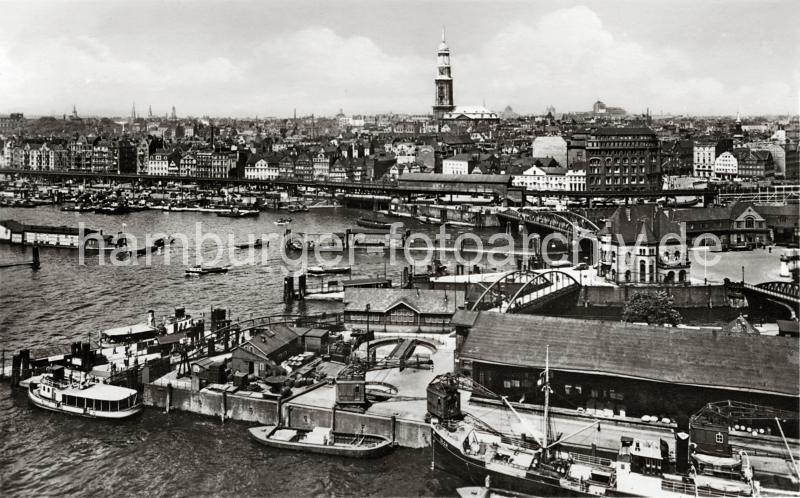 0189_236_5 Ein Dampfschiff liegt am Sandtorkai - ber Krne, die sich auf Gleisen entlang des Kais bewegen knnen, wird die Ladung des Frachters gelscht und neue Fracht an Bord gebracht. Entlang des Kais verlaufen Eisenbahnschienen - zwei Drehscheiben ermglichen das Bewegen der Gterwaggons auf engem Raum. Am Anleger des Sandtorhfts haben Hafenfhren fest gemacht. Zwischen Wilhelminenbrcke und Niederbaumbrcke das Gebude der Hafen-Polizeiwache Nr. 2 am Kehrwieder - auf der gegenber liegenden Seite des Binnenhafens die Haltestelle BAUMWALL der Hamburger Hochbahn, darunter die Einfahrt zum Herrengrabenfleet.