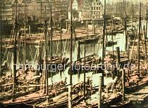 0199 Dicht an dicht liegen die Ewer und Schuten an den Holzstmmen im Binnenhafen. Mehrstckige Wohnhuser stehen auf dem Kehrwieder; am Kai sind mit Holz abgedeckte Winden zu erkennen, mit denen die Last an Land gehievt wird. Im Hintergrund die Masten der Segelschiffe im Jonashafen.