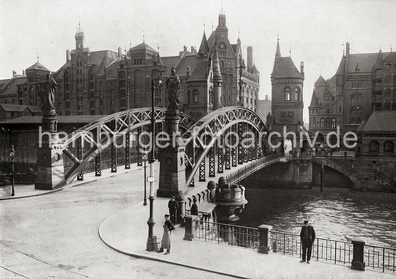 0202_017_1_32 Blick auf die Brooksbrcke ber den Zollkanal, der die Grenze zu dem Hamburger Freihafengebiet ist. Auf der Stadtseite der Brcke stehen die Figuren HAMMONIA und EUROPA auf Sockeln - auf der Speicherstadtseite befindet sich in zwei hohen neugotischen Trmen die Zollstation.  Links der Speicherblock E - auf der Strasse Kehrwieder steht ein Pferdefuhrwerk mit Kisten und Fssern beladen.