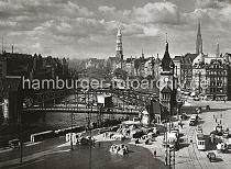 0220_056_26 Blick auf die eisernen Brckenbogen der Wandrahmsbrcke ber den Zollkanal - im Vordergrund sind Gemsekisten auf dem Gelnde des Gemsemarkts gestapelt. Lastwagen mit Planen, Handkarren und Pferdefuhrwerke stehen am Strassenrand und fahren auf der Strasse. Eine Strassenbahn fhrt Richtung Messberg, ein Radfahrer berquert die Strasse. Hinter der Kornhausbrcke der Kirchturm der St. Katharinenkirche und am rechten Bildrand die Nikolaikirche und der Turm der St. Michaeliskirche.