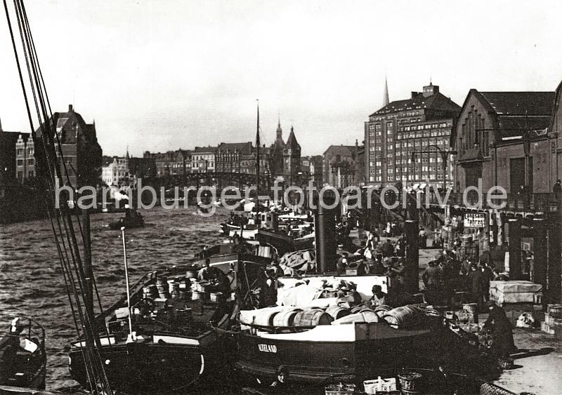 0224_221a Breite Frachtkhne liege nebeneinander am Ponton des Hamburger Gemsemarkts am Deichtor; die Ladung der Schiffe besteht aus Kisten, Krben und Holztonnen, in denen die Ware fr den Markt angeliefert wird. Rechts ein Ausschnitte einer der Gemsehallen, dahinter das Ballinkontorhaus am Messberg. Hinter den Brckenbgen der Wandrahmsbrcke beginnt der Zollkanal.