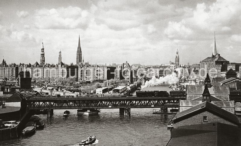 0227_056_23 Auf dem Oberhafenkanal fhrt eine Barkasse Richtung Oberhafen - auf der Oberhafenbrcke berquert eine qualmende Lokomotive mit Kohlentender und Personenwagen den Kanal. Auf der unteren Strassenebene der Drehbrcke ziehen mehrere Arbeiter ihren Handkarren. Hinter der Ericusspitze deren Inneres ein Sportboothafen birgt sind die Speicherblcke am Brooktorkai zu sehen. Die Turm der Hansestadt Hamburg v. lks.: St. Katharinenkirche, St. Michaeliskirche, St. Nikolaikirche, Rathausturm und St. Petrikirche. 