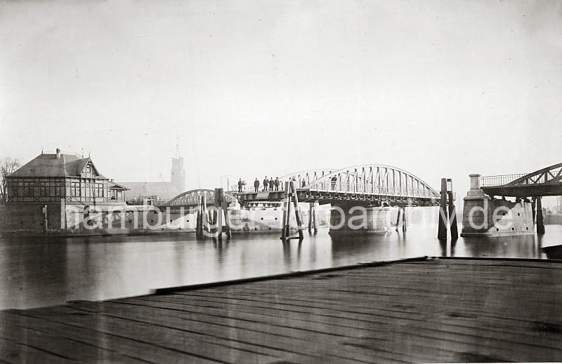 0237_39806 Blick auf die geffnete Drehbrcke am Niederhafen - Holzdalben schtzen die Brckenkonstruktion. Am Ufer ein Fachwerkhaus des Brckenwrters. Menschen stehen auf der Strasse hinter einer Schranke, die bei Brckenffnung herabgelassen wird. Im Hintergrund der Uhrenturm und Dach des Kaiserspeichers - Mastern der Schiffe auf der Norderelbe sind zu erkennen.