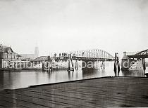 0237_39806 Blick auf die geffnete Drehbrcke am Niederhafen - Holzdalben schtzen die Brckenkonstruktion. Am Ufer ein Fachwerkhaus des Brckenwrters. Menschen stehen auf der Strasse hinter einer Schranke, die bei Brckenffnung herabgelassen wird. Im Hintergrund der Uhrenturm und Dach des Kaiserspeichers - Mastern der Schiffe auf der Norderelbe sind zu erkennen.