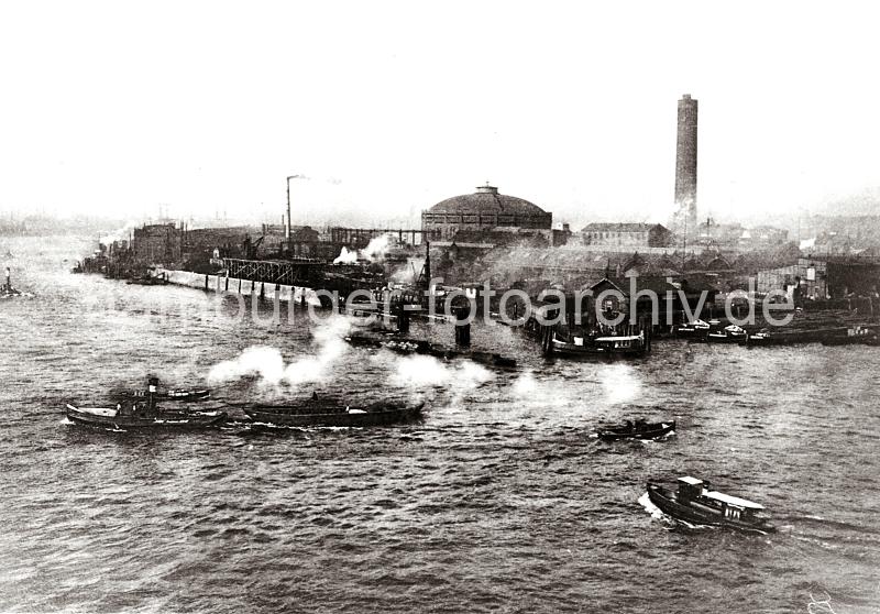 0246_XII_115 Ein Schleppverband kommt aus dem Magdeburger Hafen und berquert die Norderelbe - Binnenschiffe liegen an den Fruchtschuppen des Magdeburger Hafens. Dahinter das Gelnde der Gaswerke auf dem Grasbrook mit Gasometer und hohem Schornstein.  Das Gaswerk auf dem Grasbrook wurde 1844 als Privatgesellschaft gegrndet, schon 1845 bei einer Sturmflut zerstrt und 1846 wieder aufgebaut. 1874 ging die Anlage in den Besitz der Stadt ber. In den vier Gasbehltern  knnen insgesamt 73 000 cbm Gas gespeichert werden. Das grte Gasometer hat einen Durchmesser von 56m - es kann 50 000 cbm speichern. Die Kohle wird von Seeschiffen gebracht, die direkt am Kai des Gaswerks mit einem hydraulischen Kran entladen werden. In neun Kohlenschuppen knnen ca. 30 000 t Kohle auf dem Gelnde der Gasanstalt Grasbrook gelagert werden.