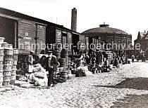 0247_XII_145 Gterwaggons aus dem der polnischen Stadt Bromberg stehen auf einem Gleis der Hafenbahn zwischen den Kaischuppen des Hbnerkais vom Grasbrookhafen und dem Strandkai der Norderelbe. Im Hintergrund die Industriearchitektur der Gasanstalt auf dem Grasbrook. Kaiarbeiter mit weissen Schrzen packen anscheinend Frchte in Krbe / Fsser um, die Ware wird mit Holzwolle gepolstert - ein Pferdefuhrwerk fhrt auf dem Kopfsteinpflaster der Hafenanlage.