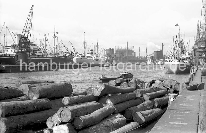 historische Hafenbilder aus dem Archiv der Hamburger Hafen und Logistik AG (HHLA) Baakenhafen, Schuten und Frachter Versmannkai  77_01 Blick ber den Baakenhafen ca. 1956; am Versmannkai liegen Schuten mit Baumstmmen beladen - ein Frachter hat an den Eisenpollern festgemacht. In der Mitte des Hafenbeckens liegen weitere Frachtschiffe an Dalben - ein Schwimmkran lscht die Ladung; im Hintergrund der Gasometer vom Gaswerk Grasbrook.