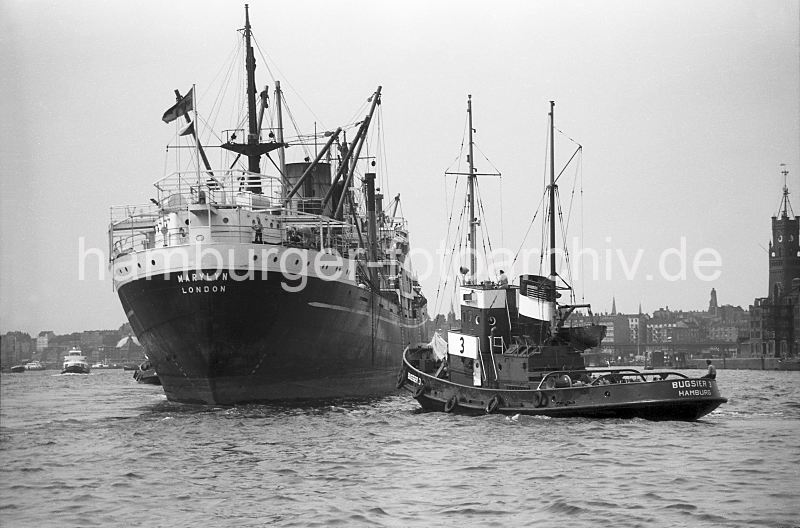 Schlepper + Frachtschiff auf der Elbe im Hamburger Hafen, 1954 180_01 Der Schlepper BUGSIER 3 untersttzt das Frachtschiff MARYLIN bei seinem Auslaufmanver aus dem Hamburger Hafen. Das Schiff kann jetzt aus eigener Kraft seinen Liegplatz verlassen; rechts im Hintergrund ein Ausschnitt der Ruine des Kaispeichers A auf dessen hohen Turm sich die Zeitballanlage befand.