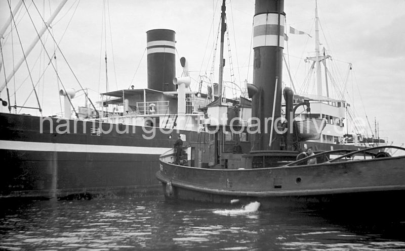 181_03 Ein Schlepper mit hohem Schornstein bugsiert das Frachtschiff an seinen Liegeplatz, in dem es den Frachter mit  seienm fendergeschtzten Bug in die gewnschte Position drckt.   Schlepper + Frachtschiff auf der Elbe im Hamburger Hafen, 1948