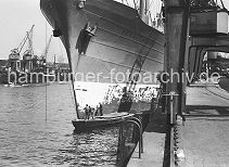 183_3 Der Frachter SCHAUENBURG liegt am Petersenkai im Baakenhafen; Matrosen des Frachtschiffs stehen auf einem Arbeitskahn und streichen den Bug des Schiffs mit Rostschutzfarbe. Im Vordergrund eine eiserne Leiter an der Kaimauer, die zum Besteigen der Khne genutzt werden kann. Daneben die Schiene, auf der die Halbportalkrane auf der Kaianlage laufen - dazwischen ein Gleis fr die Gterzge.