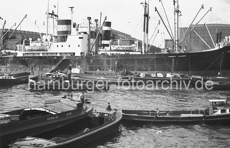 184_11 Das Frachtschiff DORA OLDENDORFF liegt in der Mitte des Rohafens an den Dalben. Schuten mit Kisten an Bord haben lngsseits fest gemacht. Im Vordergrund warten Ewerfhrer mit ihren Khnen mit Hilfe des Schleppers auf ihren Arbeitseinsatz.  Frachter + Schuten im Rohafen, 1956 - historische Hafenfotos aus dem Archiv der Hamburger Hafen und Logistik AG, HHLA. historische Hamburg Fotos als Geschenk fr Bro und Wohnung; Fotoleinwand + Posterprints. 