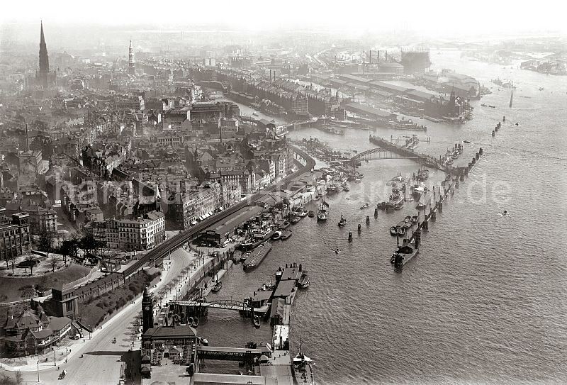 246_0259 historisches Luftbild von Hamburg; im Vordergrund lks. das St. Pauli Fhrhaus und die U-Bahnstation Landungsbrcken. am Hafentor / Vorsetzen die Speicherschuppen und Krane einer Rheinschifffahrtslinie, deren Binnenschiffe ihre Ladung ins Ruhrgebiet transportieren. In der oberen Bildhlfte fhrt die Niederbaumbrcke ber den Zollkanal zum Kehrwieder und der Speicherstadt, dahinter der Sandtorhafen und der Grasbrookhafen mit dem Kaiserspeicher. Historische Fotografien aus dem Archiv der Hamburger Hafen und Logistik AG (HHLA) Luftfoto vom historischen Hamburg / Vorsetzen, Baumwall Sandtorhafen Speicherstadt; ca. 1931