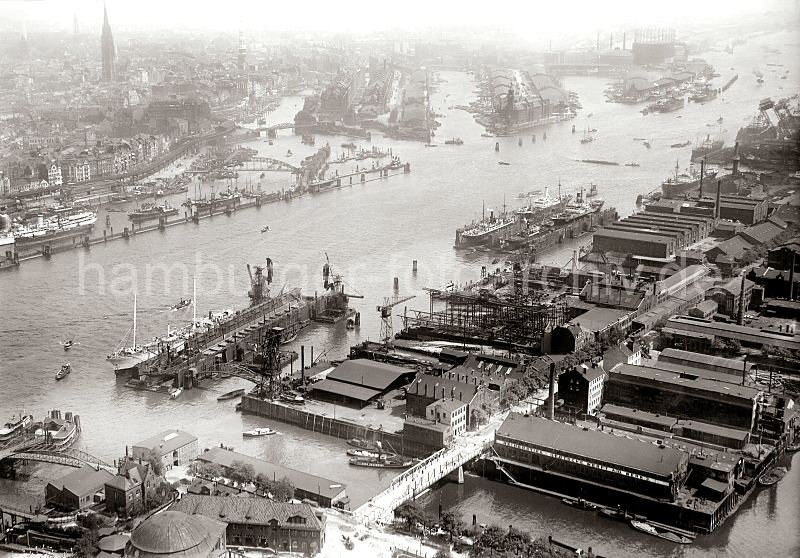 Luftbild vom historischen Hamburg / Vorsetzen, Baumwall Sandtorhafen Speicherstadt; ca. 1930 247_0409 historisches Luftbild von Hamburg; im Vordergrund lks. unten das Kuppelgebude vom Eingang des St. Pauli Elbtunnels und eine Wassertreppe zum Anleger der Hafenfhren auf Steinwerder. Hinter dem Fhrkanal das Gelnde der Stlkenwerft, davor zwei Schwimmdocks. Auf der anderen Seite der Elbe der Binnenhafen und die Lagerhuser der Speicherstadt. Rechts der Sandtor- und Brooktorhafen - im Hintergrund der Gasometer der Gasanstalt auf dem Grossen Grasbrook; davor Lagerschuppen am Strandkai.