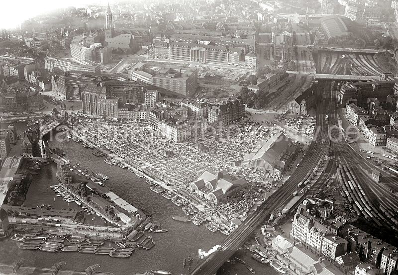 248_0136 historisches Flugbild von Hamburg; unten fhrt gerade ein Zug ber die Oberhafenbrcke Richtung Hamburger Hauptbahnhof. Neben den Bahngleisen die Deichtorhalle - auf dem Gelnde findet der Gemsemarkt statt; dicht gedrngt sind die Verkaufsstnde aufgestellt. Im linken Bildzentrum das Kontorhausviertel mit Ballinhaus und Chilehaus - dahinter das Karstadt-Verwaltungsgebude an der Steinstrasse; rechts davon das Naturhistorische Museum. Links unten die Ericusspitze, eine ehem. Bastion  der Hamburger Verteidigungsanlagen.Historische Hamburgmotive aus dem Archiv der Hamburger Hafen und Logistik AG (HHLA) Flugbild vom alten Hamburg / Oberhafen, Ericusspitze - Deichtormarkt; ca. 1931