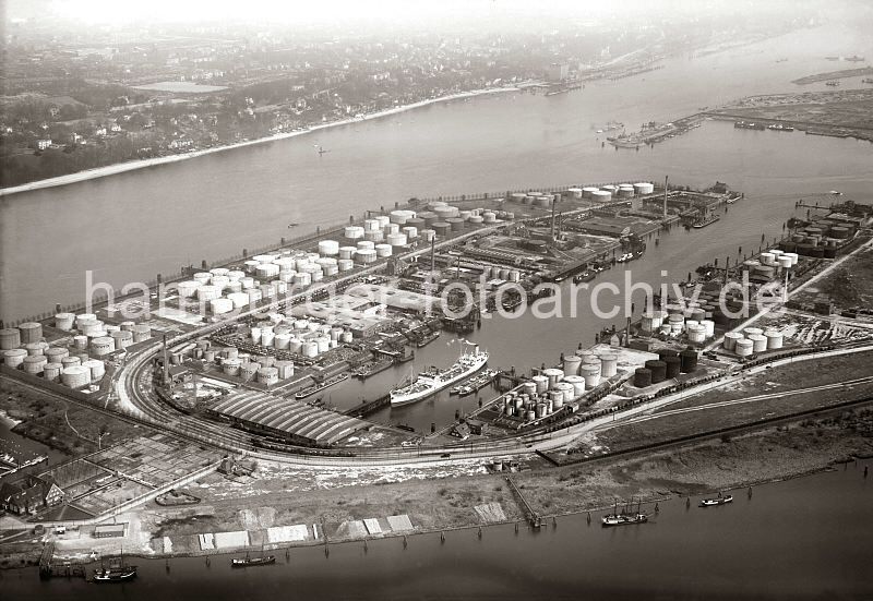 Historische Hafen-Bilder aus dem Archiv der Hamburger Hafen und Logistik AG (HHLA)Flugbilder vom Hamburger Hafen - Petroleumhafen, Waltershof - Elbe, Oevelgnne: ca. 1931  276_2523 Blick ber den Petroleumhafen Waltershof; ein Tanker liegt im Hafenbecken und wird gelscht. Auf dem gesamten Hafengelnde stehen unterschiedlich grosse runde Tanks., Auf der gegenber liegenden Seite der Einfahrt des Tankhafens der Parkhafen mit dem Athabaskahft. Am anderen Elbufer die Huser von Oevelgnne und das hohe Khlhaus in Neumhlen.