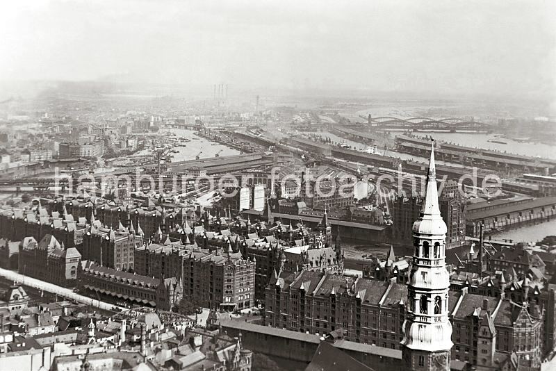 Luftansicht der Hamburger Speicherstadt - Magdeburger Hafen, Oberhafen; ca. 1930 281_0719 Blick ber die Dcher mit den Giebeltrmen der Lagerhuser in der Hamburger Speicherstadt - im Vordergrund der Kirchturm der Hamburger Hauptkirche St. Katharinen. An der Spitze des kupfernen Barockhelms des Kirchturm ist die Goldkrone der Heiligen Katharina zu erkennen. Direkt dahinter der Kaischuppen B am Magdeburger Hafen. Links der Oberhafenkanal, der zum Billehafen und zur Norderelbe fhrt. Im Bildzentrum das Abfertigungsgebude vom Hannoverschen Bahnhof am Lohseplatz. Im Hintergrund die vier markanten Schornsteine des Kraftwerks Tiefstack an der Billwerder Bucht. Rechts die Freihafenelbbrcke und die Norderelbrcke.