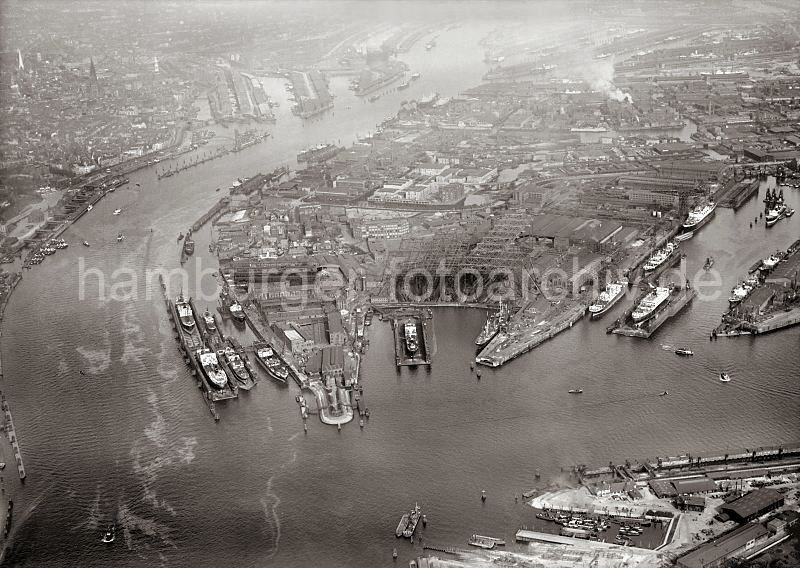 Flugbild vom Hafen Hamburg - Werft Blohm & Voss, Elbe St. Pauli Landungsbrcken; ca. 1930alte Hamburg Fotos als Print oder Fotoposter / fotoleinwand - Kunstdruck.  282_0995 Im Bildzentrum das Werftgelnde von Blohm & Voss; Schiffe liegen zur Reparatur in den Schwimmdocks. Rechts der Kuhwrder Hafen mit dem Steinwrder Ufer und dem Grevenhofer Ufer, sowie dem Kaiser-Wilhelm Hft. Am linken Bildrand die Anleger der St. Pauli Landungsbrcken und im oberen Bildzentrum der Binnenhafen mit der Einfahrt zum Zollkanal sowie den Kaischuppen am Sandtorhafen und Grasbrookhafen.