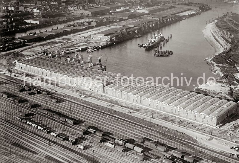  - als Kunstdruck, Fotoposter / Fotoleinwand. Luftbilder vom Hafen Hamburgs -Sd West Hafen;  Winkhukkai, Kamerunkai; ca. 1932 296_3279 Luftfoto vom Windhukkai des Sd-West-Hafens,  dem Lagerschuppen 59  mit den Tonnengewlben am Veddeler 9amm und den Gleisanlagen des Gterbahnhofs Hamburg Sd. Ein Frachter liegt an den Dalben in der Mitte des Hafenbeckens, die Fracht wird ber Schuten gelscht. Am Togo Kai noch keine Kaibefestigung errichtet, whrend am Kamerun Kai die Kaischuppen 60,61 und 62 mit Krananlagen stehen -  dahinter der Grenzkanal.