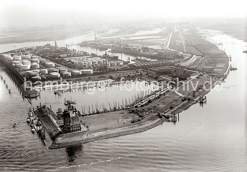 Historische Hafenfotos aus dem Bildarchiv der Hamburger Hafen und Logistik AG (HHLA) Luftbilder vom Hafen Hamburg - Jachthafen Waltershof - Lotsenhaus, Petroleumhafen; ca. 1931 302_0267 Luftbild von Waltershof; im Vordergrund das Lotsenhaus, mit dem Uhrturm dessen Backsteinarchitektur der Hamburger Oberbaudirektor Fritz Schumacher entworfen hat. Lotsenschiffe liegen am Seemanns Hft. Dahinter die Einfahrt zum Finkenwerder Jachthafen, der Entwurf des Vereinshauses im Landhausstil ebenfalls vom Architekten Schumacher stammt. Rechts das Khlfleet mit der Eisenbahnbrcke, die zur Dradenau fhrt; lks. davon das halbfertige Hafenbecken des Griesenwrder Hafen und der Waltershofer Hafen. Links am Bubendey Ufer die Tanklager des Petroleum Hafens.