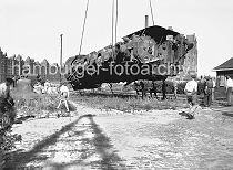 441_03 Eine im Krieg zerstrte Lokomotive wird 1948 von einem Kran im Sandtorhafen geborgen; im Hintergrund die Gebude der Speicherstadt am Brooktorkai - rechts ist ein Ausschnitt des Kaispeichers B zu erkennen. Die Kirchenglocken im linken Bildrand wurden whrend der Kriegszeit auf Befehl in den Kirchentrmen abgehngt und teilweise auch im Freihafen zwischengelagert - sie sollten eingeschmolzen werden.