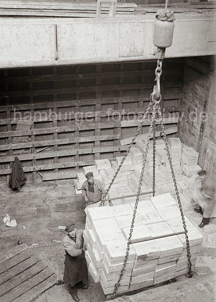 historische Bilder von der Arbeit im Hamburger Hafen; ca. 1932. Alte Hafenbilder aus dem Fotoarchiv der Hamburger Hafen und Logistik AG. 469_576 Die Ladung Rosinenkisten ist von den Stauern auf dem Ladegeschirr des Krans verstaut und wird aus dem Laderaum des Frachters gehievt.