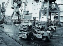 495_01 Der Gabelstaplerfahrer hat zwei Paletten mit Scken auf seinen Gabeltrger aufgenommen und fhrt seine Last ber die Kaianlage im Hamburger Hafen - im Hintergrund werden Container mit einen Kran auf das am Kai liegende Frachtschiff verladen.