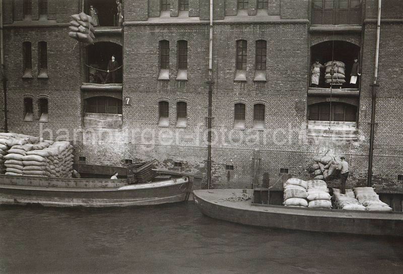 historische Motive der Hamburger Speicherstadt - Bildarchiv der Hamburger Hafen und Logistik. Hafenbilder auf Fotoleinwand mit Rahmen oder Poster zum schenken fr Weihnachten, Geburtstag, Jubilaeum oder zur Dekoration.  499_3502_109 Warenumschlag in der Speicherstadt - die Ladung zweier Schuten wird gelscht. Mit den Winden, die unter den Dchern der Speichegebude befinden, werden die Scke auf die Bden der Lagerrume gebracht.