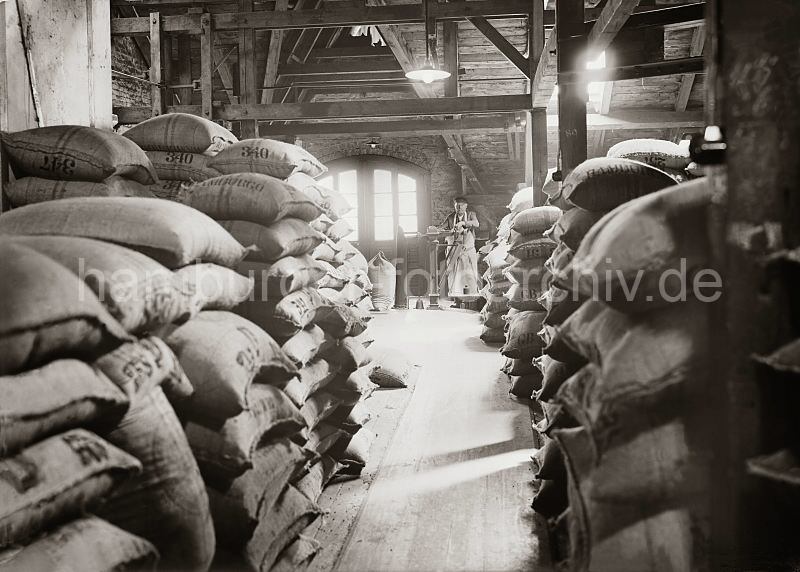 Quartiersmann mit Waage - Kaffeeboden in der Hamburger Speicherstadt; ca. 1938. Alte Hamburg-Motive als Kunstdruck zum Geburtstag, Jubilaeum, Abschiedsgeschenk oder zu Weihnachten. 504_271a Ein Quartiersmann steht an der Waage auf dem Speicherboden im Hamburger Freihafen. Der Rohkaffee ist in Jutescken vernht, die auf dem Lagerboden des Speichers gestapelt sind. Schon 1885 wurde mit der Planung zum Bau der Hamburger Speicherstadt begonnen. Es entstand unter der Leitung des zustndigen Oberingenieurs Franz Andreas Meyer in neogotischer Architektur auf einer Gesamtflche von 630 000 der grte zusammenhngende Lagerkomplexes der Welt. Betrieben wurden die Speichergebude von der HFLG, der Hamburger Freihafen-Lagerhaus-Gesellschaft, aus der 1935 nach dem Zusammenschluss mit der Hamburger Kaiverwaltung die Hamburger Hafen- und Lagerhaus Aktiengesellschaft HHLA entstand.