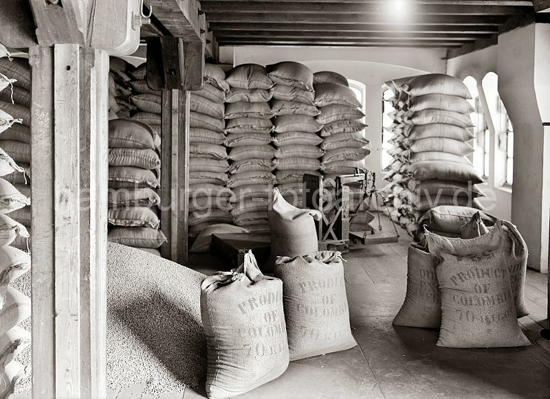 Scke mit Kaffee aus Kolumbien - aufgeschtteter Rohkaffe, Lastwaage - Speicherstadt Hamburg; ca. 1938</font>. Alte Hamburg-Motive als Poster zum Geburtstag, Jubilaeum, Abschiedsgeschenk oder zu Weihnachten.  505_505a Der Kaffee aus Kolumbien ist in Jutescke vernht und bis an die Decke des Speicherbodens gestapelt. Die Scke tragen die Aufschrift Produkt of Colombia - 70 Kilos. Ein Haufen Kaffee ist auf dem Lagerboden ausgeschttet - im Hintergrund eine Waage, mit der die Scke gewogen werden.