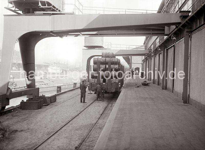 Alte Bilder aus dem Hafen Hamburgs - Fotoarchiv der Hamburger Hafen und Logistik AG (HHLA)- Halbportalkrne am Kaiserkai im Hamburger Sandtorhafen - Gterzug mit Fssern beladen.  511_430 Ein mit Fssern beladener Gterzug steht an der Laderampe eines Schuppens am Kaiserkai des Sandtorhafens. Darber laufen die Portale der Krane - neben der Gleisanlage der Hafenbahn ist noch die Schiene zu erkennen auf der alten Hafenkrne gelaufen sind. 511_430 Ein mit Fssern beladener Gterzug steht an der Laderampe eines Schuppens am Kaiserkai des Sandtorhafens. Darber laufen die Portale der Krane - neben der Gleisanlage der Hafenbahn ist noch eine der Schienen zu erkennen, auf denen die alten Hafenkrne gelaufen sind.