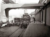 513_431 Lastwagen werden an der Rampe des Lagerschuppens am Kaiserkai beladen - ein Hafenarbeiter schiebt eine Sackkarre mit Scken an die Ladeflche des LKW ein anderer Arbeiter ldt das Sackgut auf. Ein weiterer Lastkraftwagen wartet neben einem mit Metallfssern hoch beladenen Gterwaggon der Hafenbahn. Im Hintergrund sind die Frachtschiffe am Sandtorkai und der Kaispeicher B zu erkennen. 