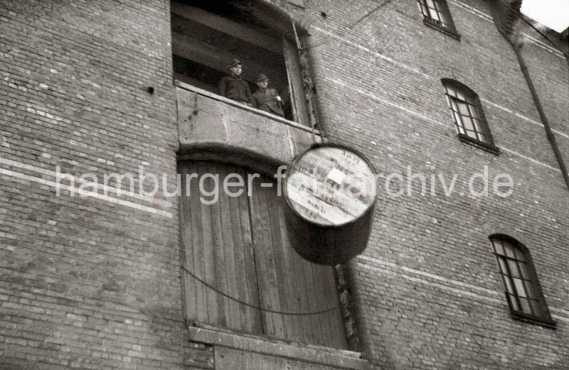 Historische Hamburgfotografien aus dem Hafen - Bildarchiv der Hamburger Hafen und Logistik AGd HHLA - Gterumschlag im Saalehafen, Dessauer Ufer - Lagerhaus G, Holzfass am Kranhaken; 1948.  517_0002 Das grosse Tabakfass wird zur Ladeluke des Kaispeichers G am Dessauer Ufer des Saalehafens hoch gezogen - zwei Arbeiter erwarten auf dem Lagerboden das Fass, um es durch die Luke herein zu ziehen.