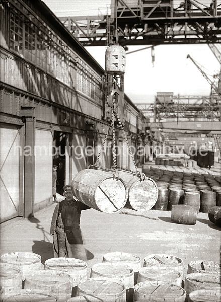 Alte Hafenfotos - Bildarchiv der HHLA - Verladung von Holztonnen am Ladegeschirr - Laderampe; ca. 1930.  518_425 Zwei Holzfsser hngen im Ladegeschirr am Haken des Halbportalkrans im Hamburger Hafen. Weitere Tonnen stehen auf der Laderampe - im Hintergrund Gterwaggons der Hafenbahn.