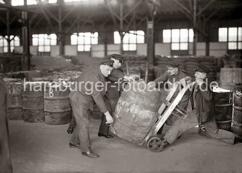 Alte Hamburger Hafenbilder - Lagerarbeiter setzen ein Fass auf eine Handkarre - Lagerraum im Hamburger Kaischuppen; ca. 1930. 519_422 Von Hand setzen die Lagerarbeiter ein schweres Holzfass auf eine Transportkarre - zwischen den Handgriffen befindet sich ein Eisenbgel, der ein Durchrutschen der Tonne verhindert. Im Lagerraum des Hamburger Kaischuppens sind Tonnen und Scke gelagert.