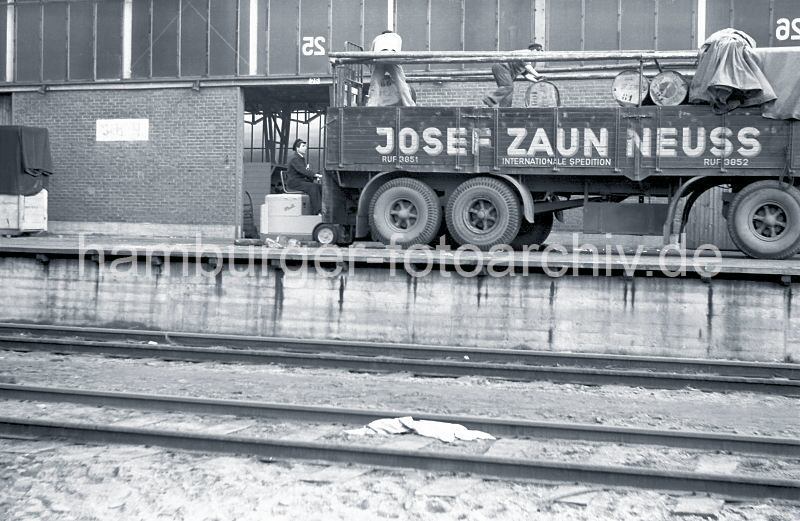 Fotografien zur Geschichte des Hamburger Hafens - Bilder aus dem Fotoarchiv der HHLA // Fsserverladung im Hamburger Sdwesthafen, Togokai - Gabelstapler und Lastwagen-Anhnger; 1952.  522_0003 Der Gabelstaplerfahrer hat die Fsser auf der Ladeflche des LKW-Anhngers abgeladen - zwei Arbeiter rollen die Metalltonnen auf dem Anhnger der Spedition, um sie sicher zu verstauen. Im Vordergrund Eisenbahnschienen der Hafenbahn vor der Laderampe.