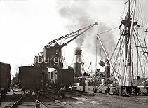 540_138 Ein Frachter liegt an der Kaimauer des Holthusenkais in der Norderelbe - über einen Portalkran wird das Schiff mit Säcken beladen. Auf den Gleisen der Bahnanlage stehen die Güterwaggons von denen die Fracht auf das Frachtschiff geladen wird. Historische Motive aus dem Hamburger Hafen, Freiladeverkehr am Holthusen