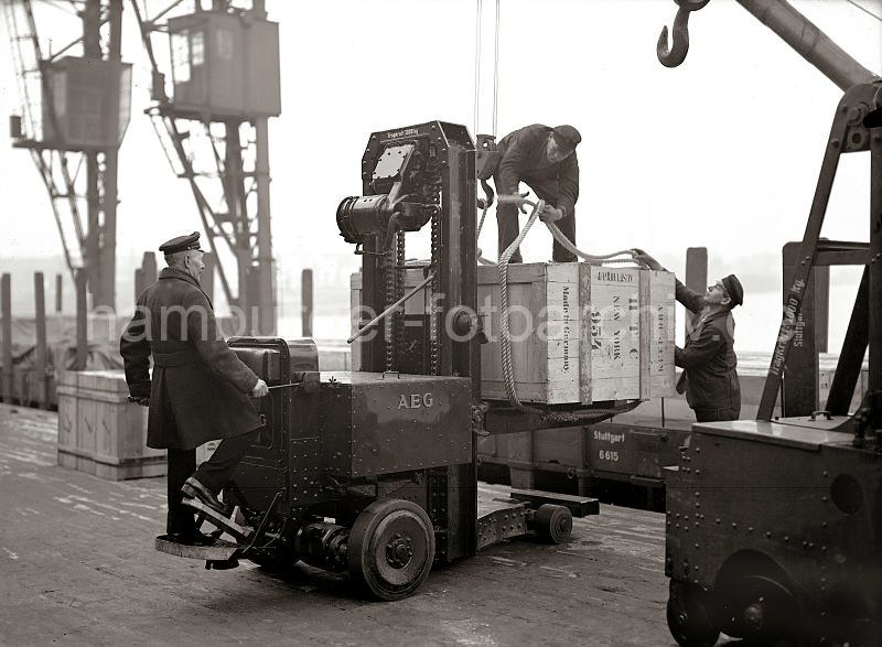 Historische Bilddokumente aus dem Hafen / Fotoposter und Bilder auf Leinwand als Hamburggeschenk. Hamburger Hafen-Fotoarchiv. Hubkarre der AEG mit Kiste beim Schuppen 83 / Chilekai, Oderhafen; ca. 1934.  543_184 Eine groe Holzkiste ist mit einem Elektrohubwagen der AEG von seinem Fahrer auf die Rampe des Schuppen 83 am Chilekai des Hamburger Oderhafens transportiert worden. Hafenarbeiter legen Tauwerk um die Kiste, an dem der fahrbare Kran sie auf den bereitstehenden Gterwaggon heben wird.